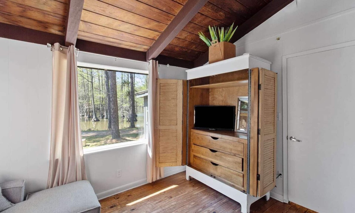 Shreveport Cabin | Emerald Cottage offers a laid-back stay surrounded by towering trees, with a spacious deck, kayaks and canoes to paddle through the cypress forest, and a firepit perfect for slow evenings outside.