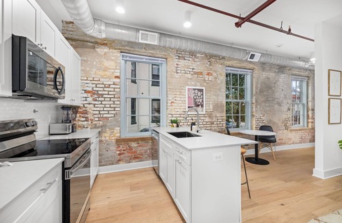 Old Town Alexandria Apartment | Design-forward flat in Old Town's most iconic building. Exposed brick, bold red ceiling pipes, corner bedroom bathed in natural light. Modern kitchen, quiet side street. Steps from 100+ restaurants & waterfront. A LovableBNB Collection listing.