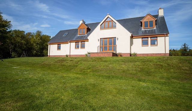 Family house surrounded by lawn and woodlands with countryside views.