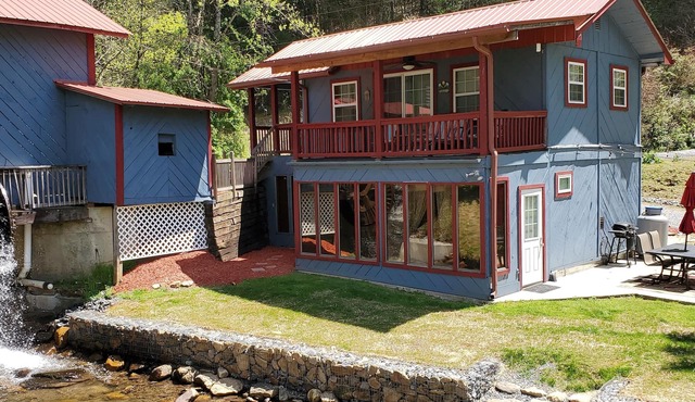 Rustic two-story cabin on creek with covered bridge and water wheel.